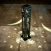 Decorative outdoor garden column with tree and moon design casting shadows on a concrete surface
