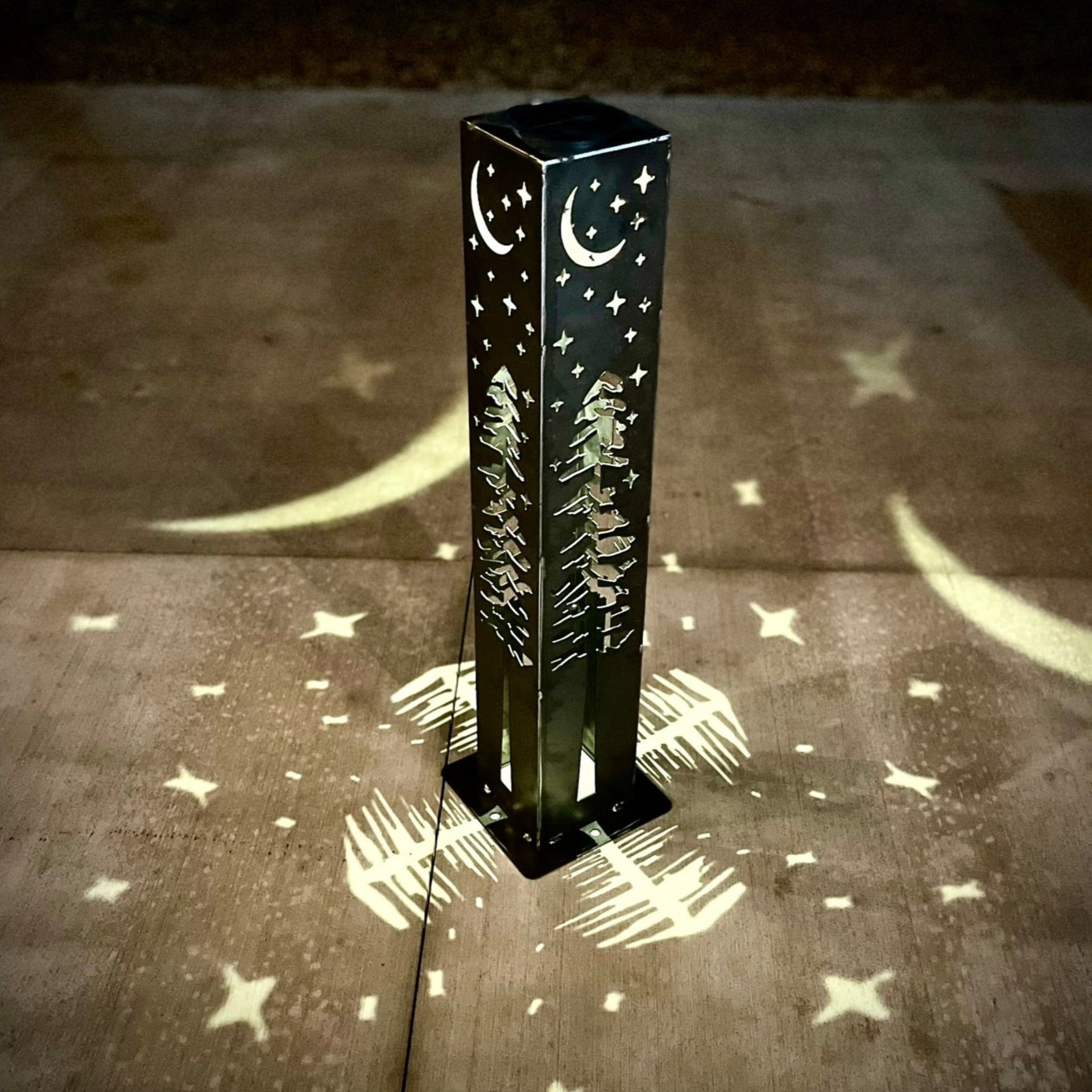 Decorative outdoor garden column with tree and moon design casting shadows on a concrete surface