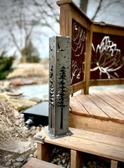 Decorative garden column with tree and moon design on a wooden bench by a water body.