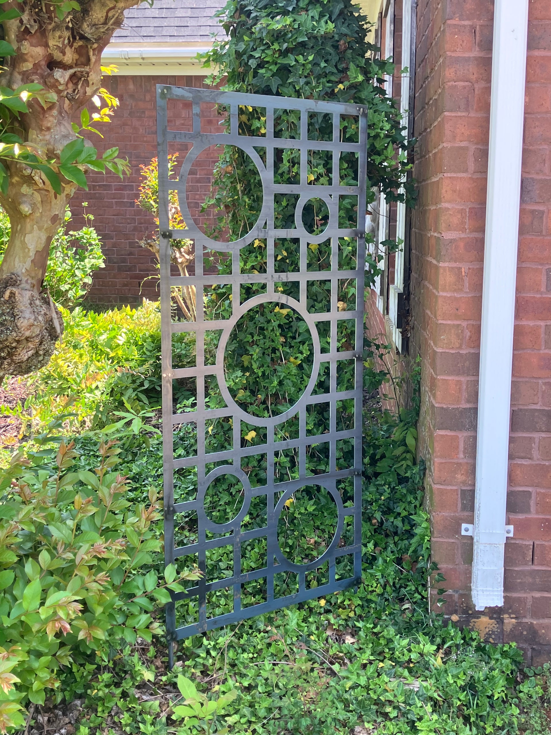 Decorative metal trellis on a brick wall with greenery