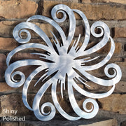 Decorative metal wall art with swirling design on a stone wall, labeled 'Shiny Polished'.