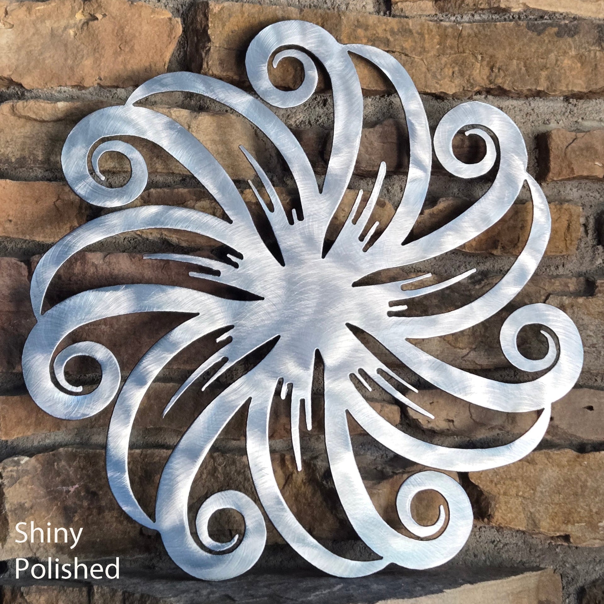 Decorative metal wall art with swirling design on a stone wall, labeled 'Shiny Polished'.