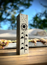 Decorative metal pillar with a sunflower design on a wooden surface outdoors.