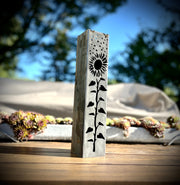 Decorative metal garden pillar with sunflower design on a wooden surface outdoors