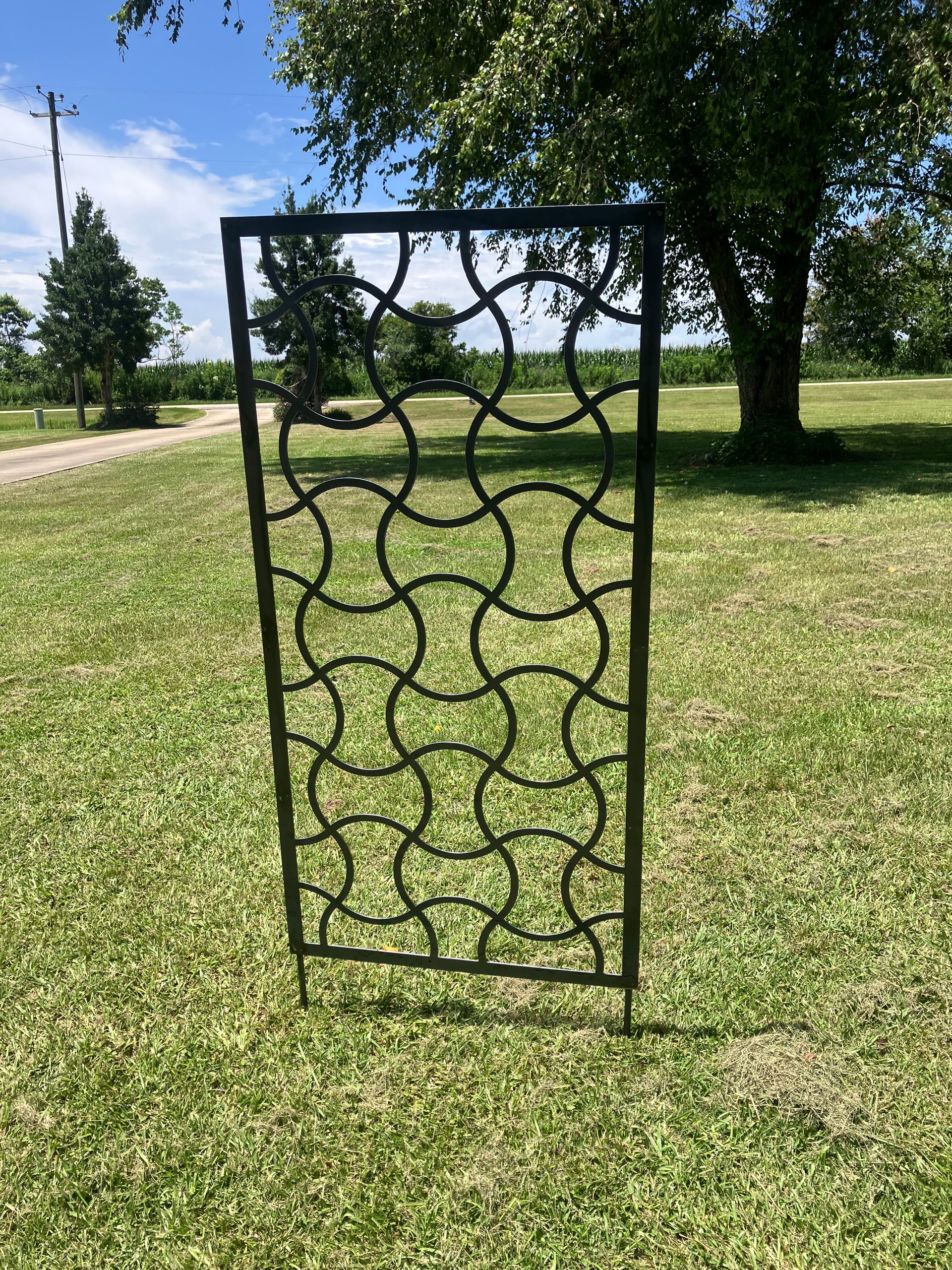 Decorative metal screen on grass with trees and sky in the background