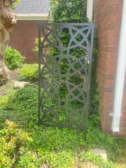 Decorative metal screen in a garden setting with greenery and a brick wall.