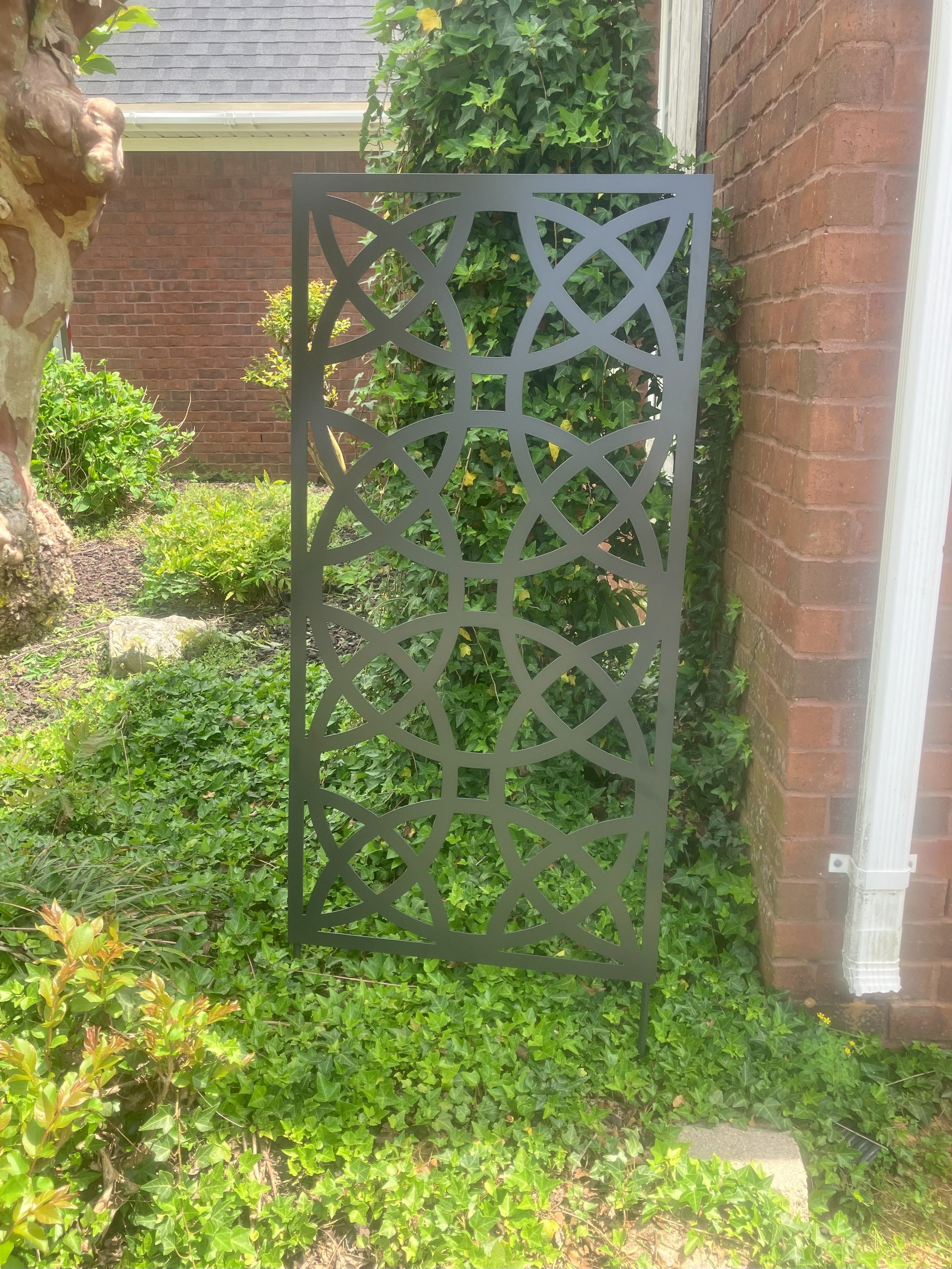 Decorative metal screen in a garden setting with greenery and a brick wall.