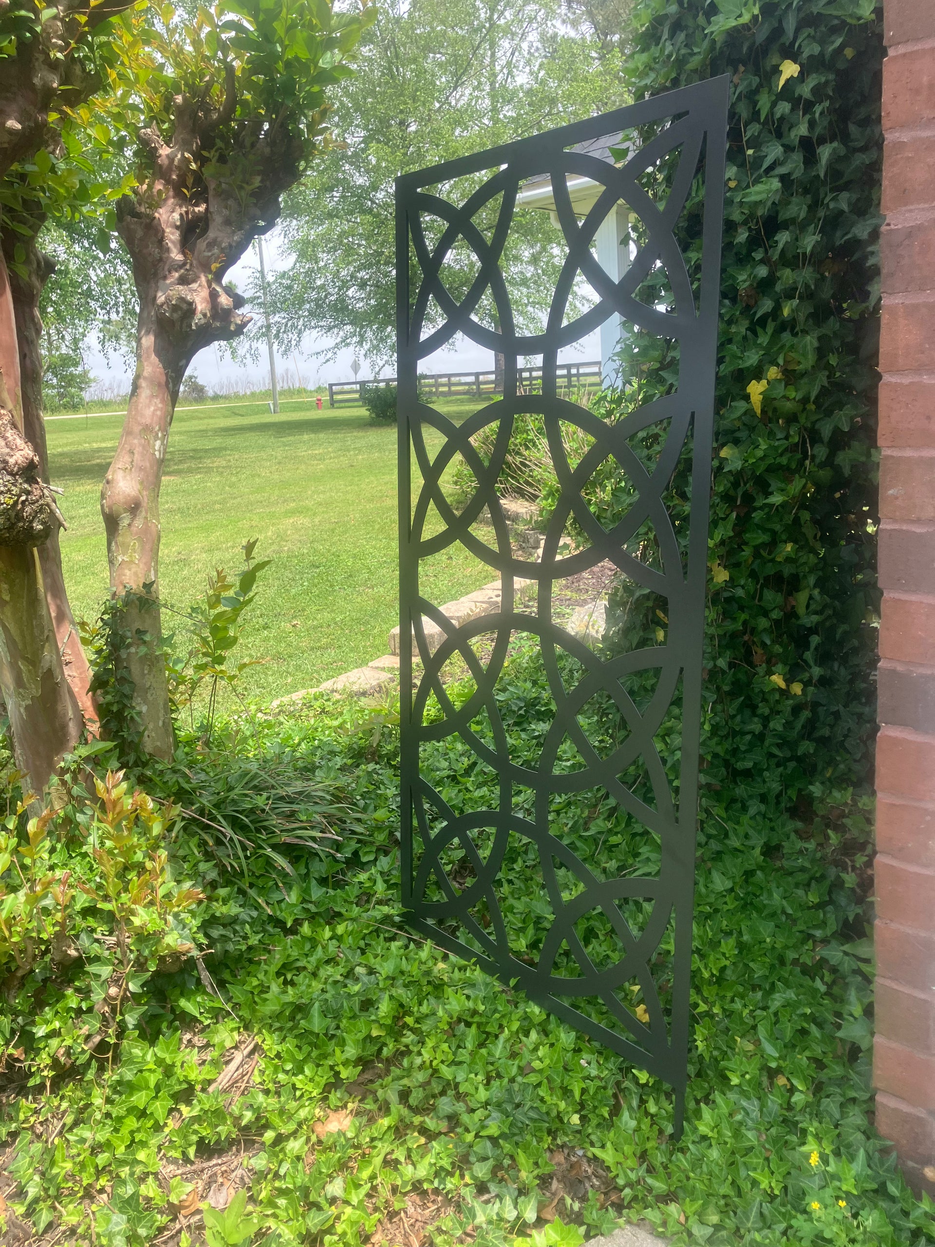 Decorative metal screen in a garden setting with greenery and a brick wall.