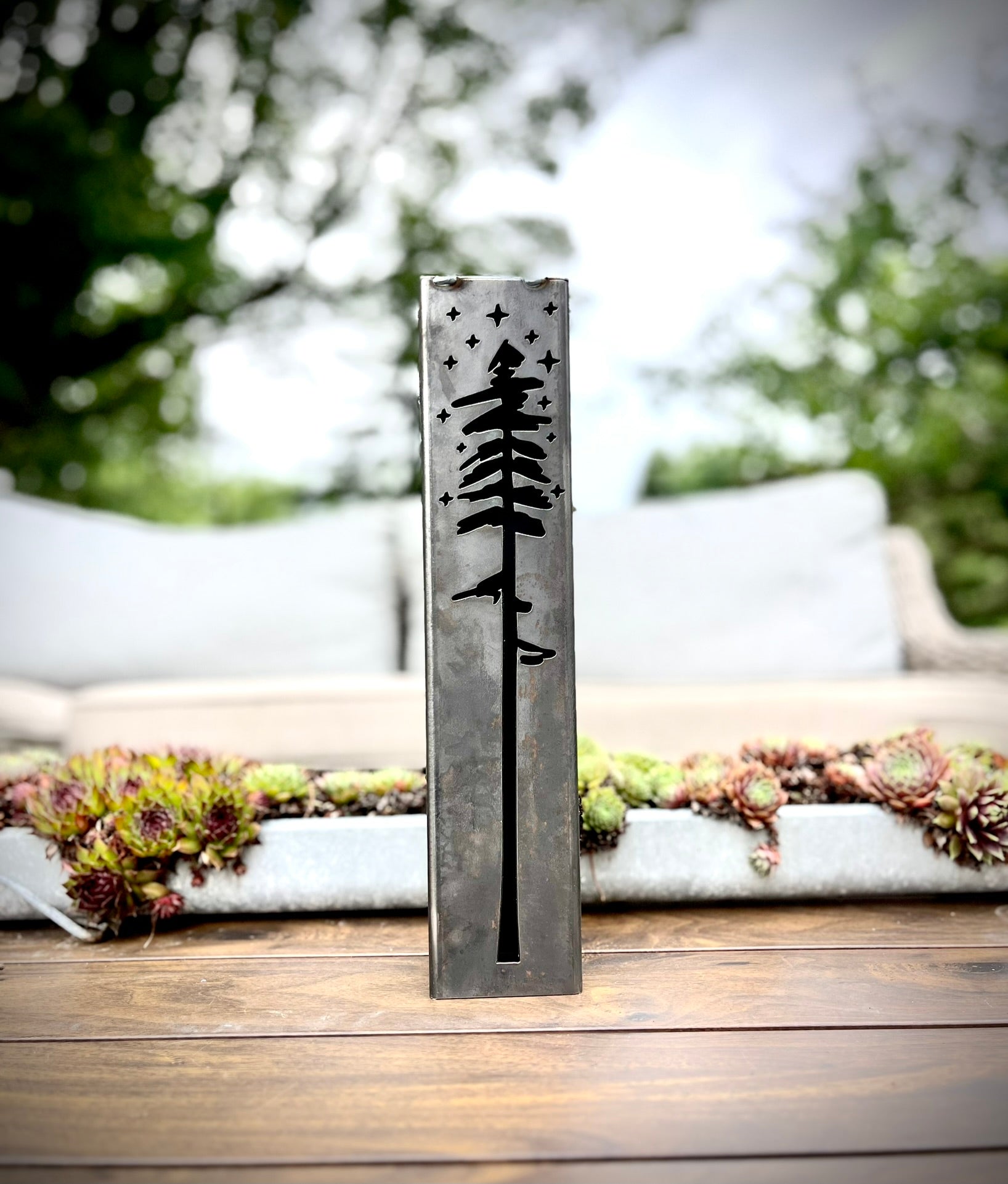 Decorative metal pillar with tree design on a wooden surface outdoors