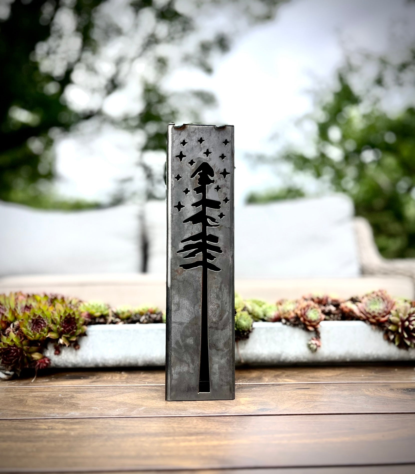 Decorative metal pillar with engraved design on a wooden surface outdoors.