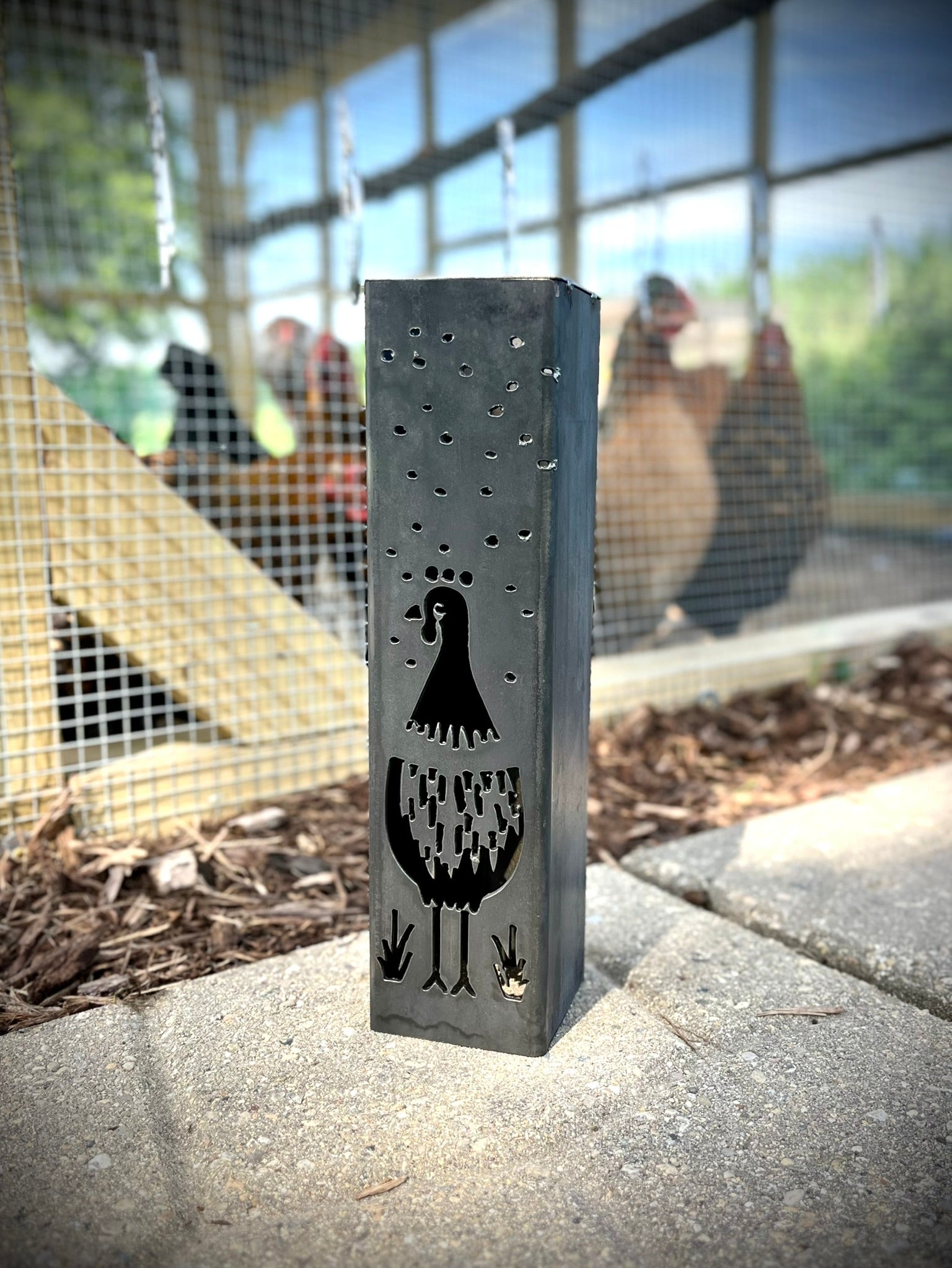 Garden Column Pillar with cut-out design on a concrete surface, with chickens in the background.