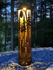 Decorative outdoor garden pillar with cut-out designs of trees and deer in a forest setting.