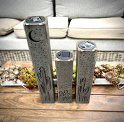 Three decorative metal pillars with cactus designs on a wooden surface.