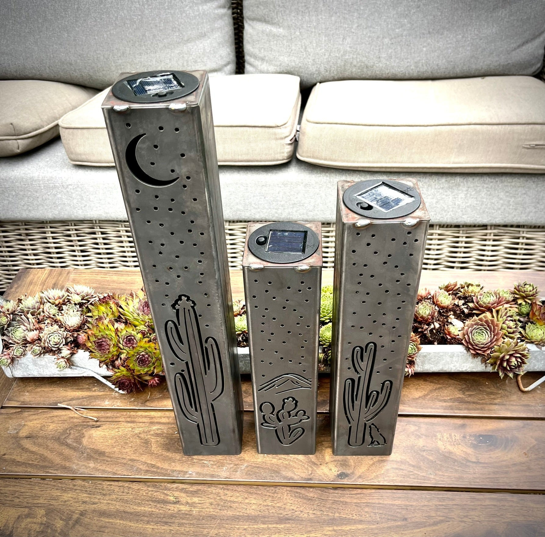 Three decorative metal pillars with cactus designs on a wooden surface.