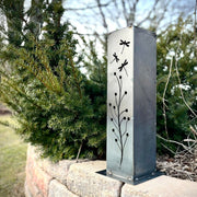 Decorative metal garden pillar with dragonfly design in a garden setting