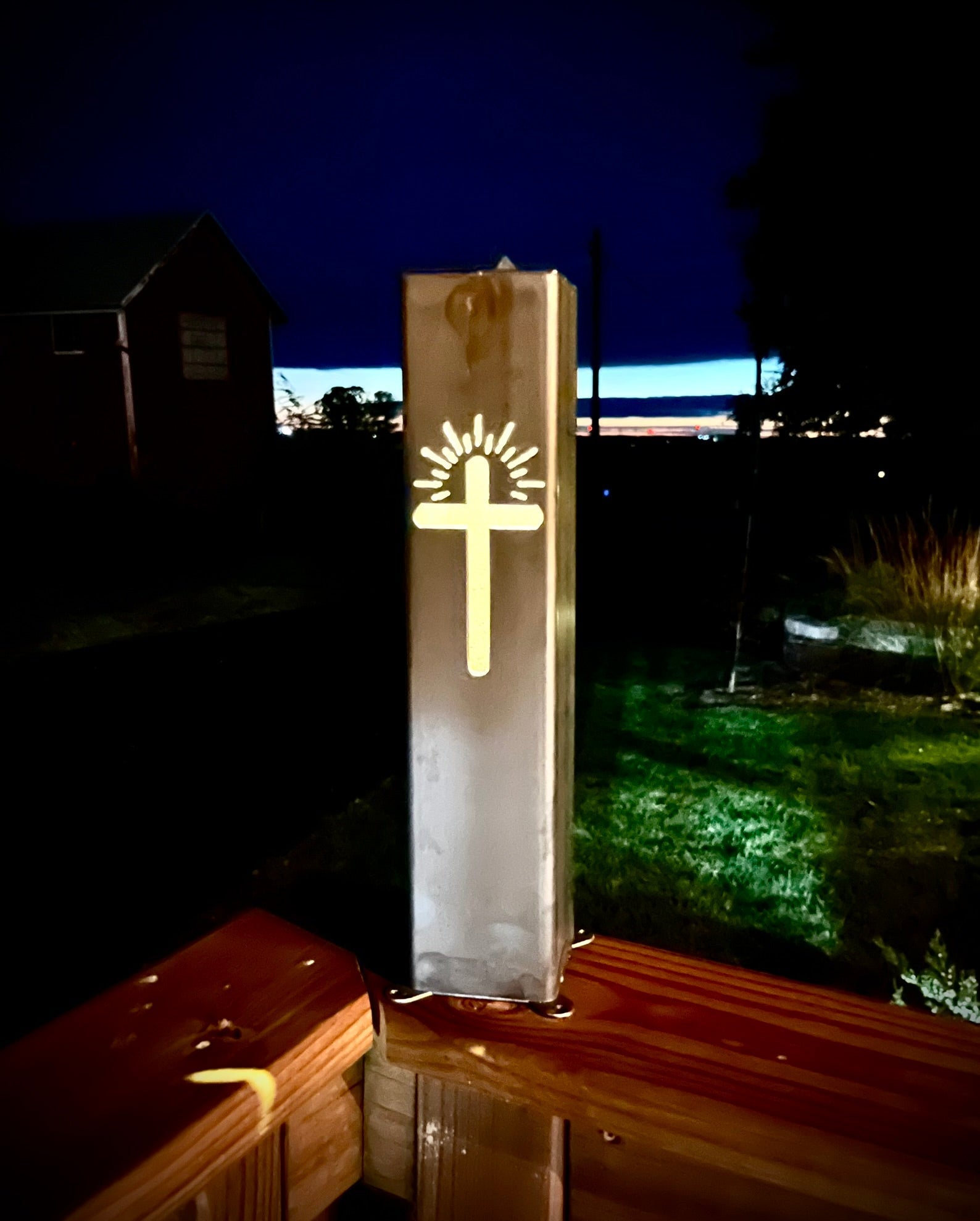 Decorative Garden Column Pillar fixture with cross design on a wooden surface at night.