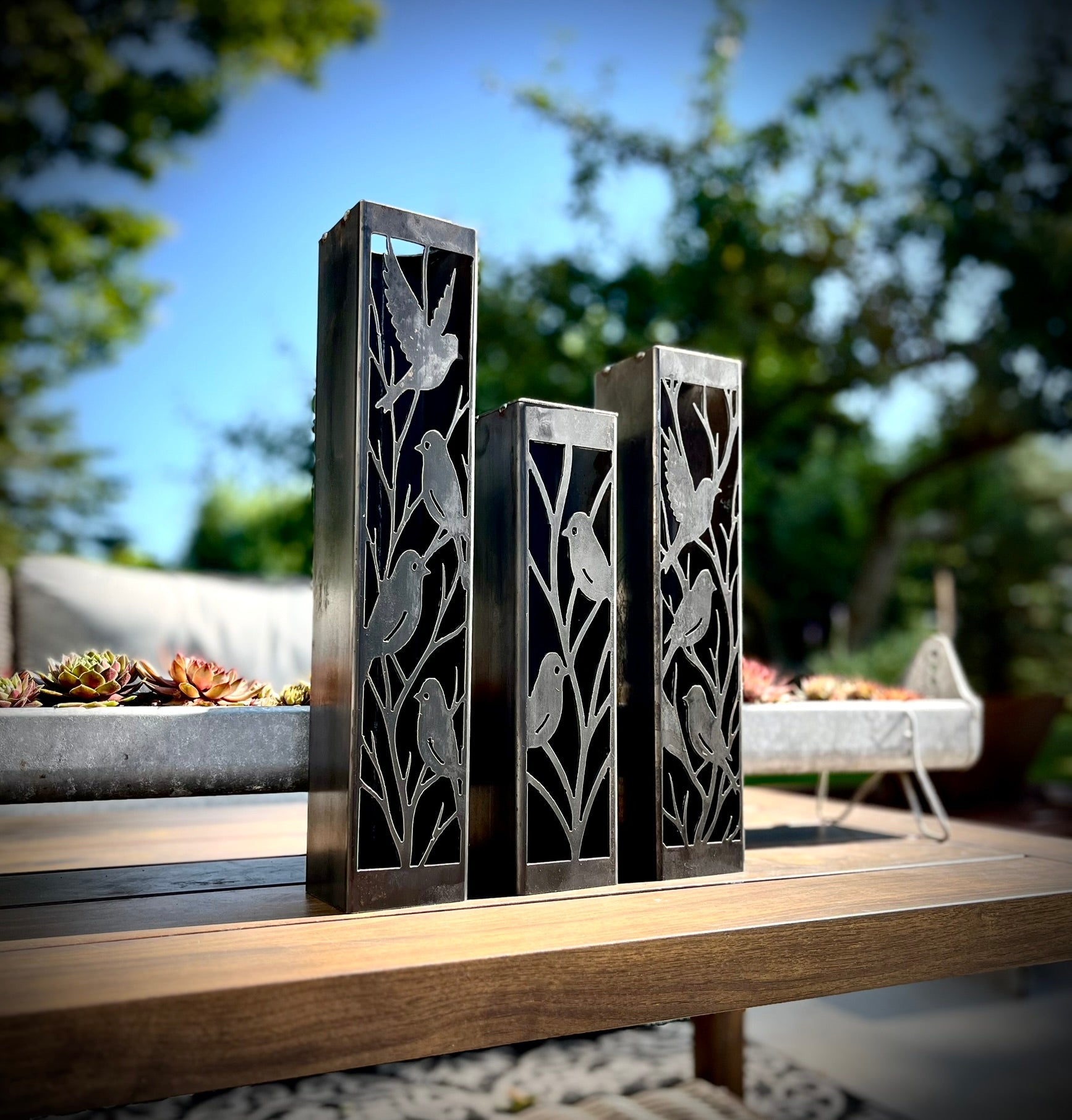 Outdoor Decorative Columns with bird cutouts on a wooden surface outdoors.