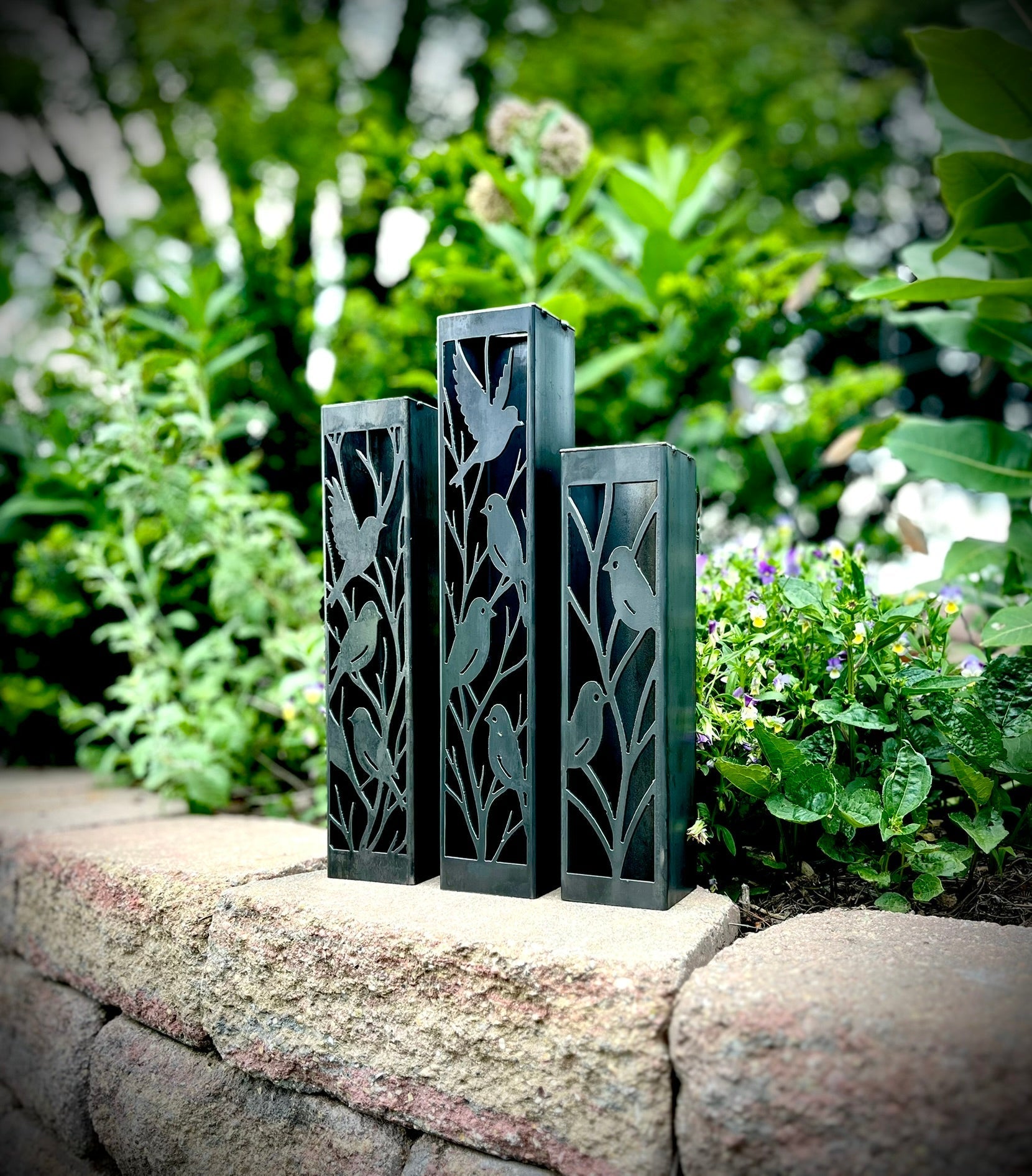 Outdoor Decorative Columns with bird patterns on a stone ledge with greenery in the background