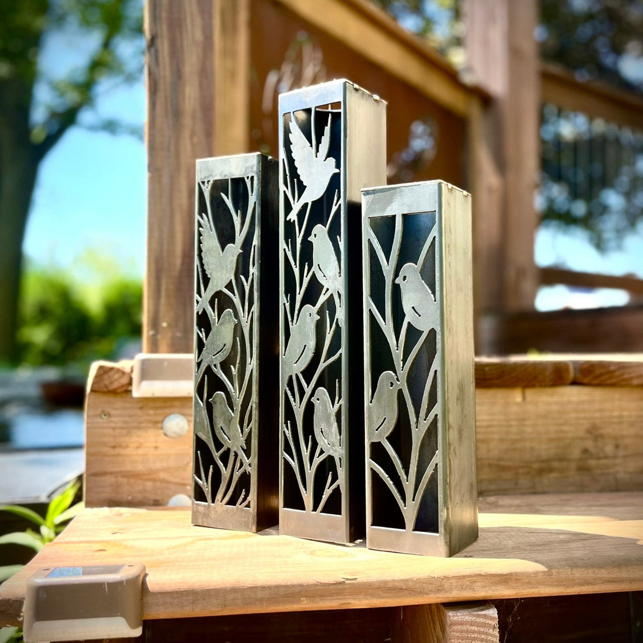 Three Outdoor Decorative Columns with bird cutouts on a wooden surface outdoors.