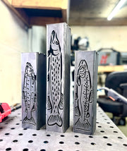 Three metal garden column pillars with fish designs on a pegboard in a workshop setting.