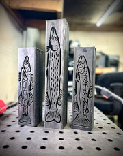 Three metal garden column pillars with fish designs on a workshop table.