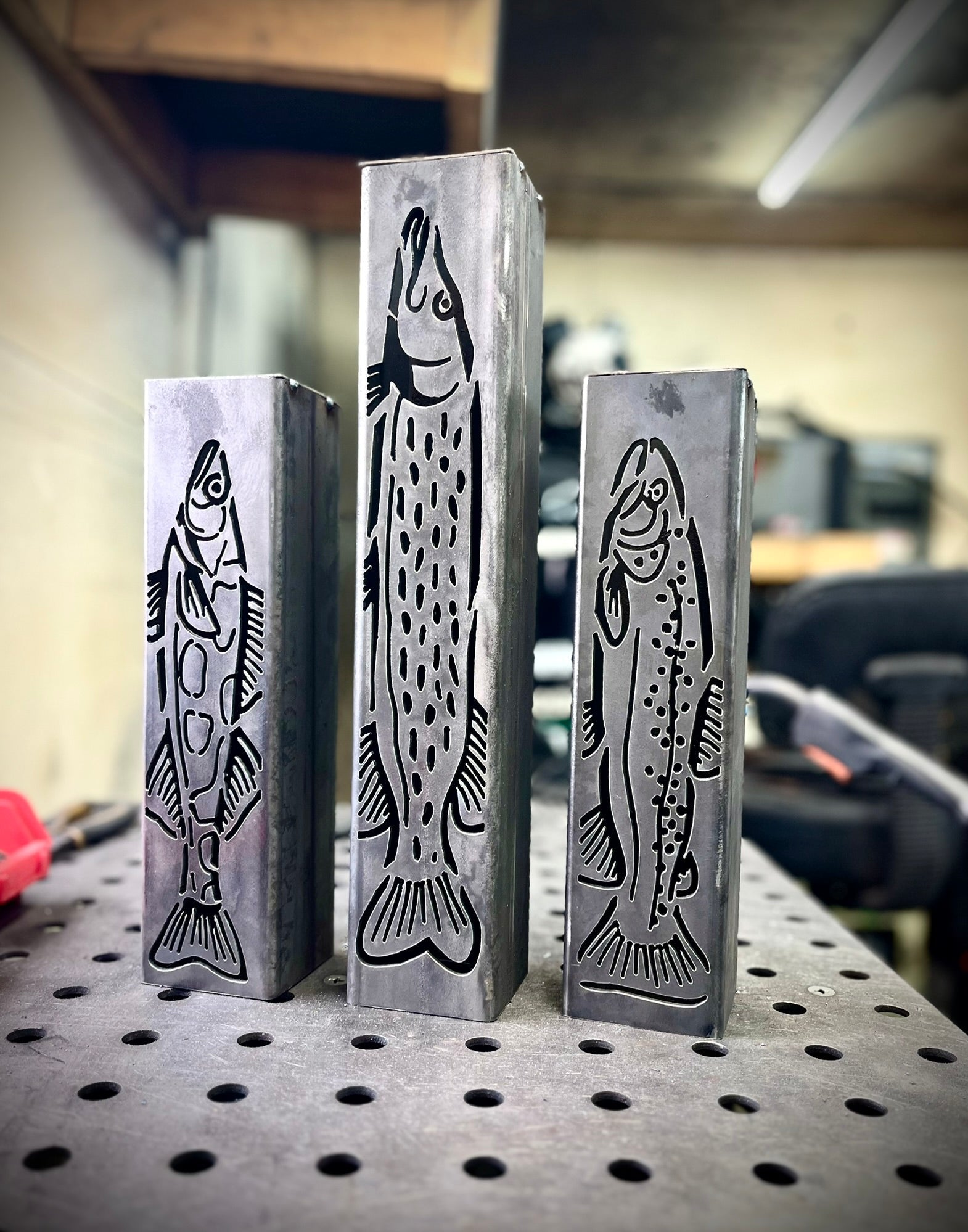 Three metal garden column pillars with fish designs on a workshop table.
