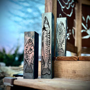 Three metal garden column pillars with fish designs on a wooden surface.