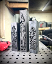 Three metal garden column pillars with fish designs on a workshop table.