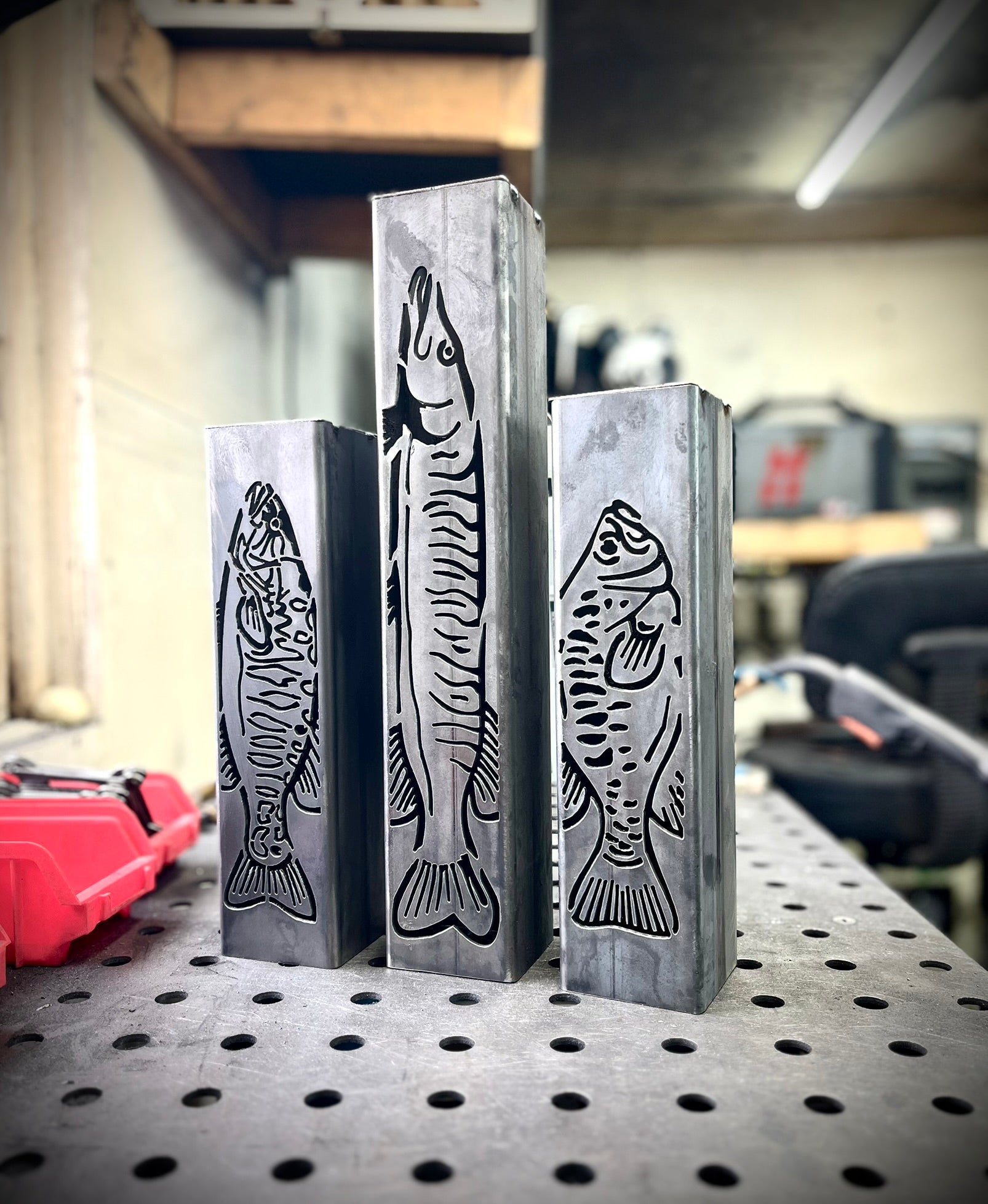 Three metal garden column pillars with fish designs on a workshop table.