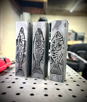 Three metal garden column pillars with fish designs on a workshop table.