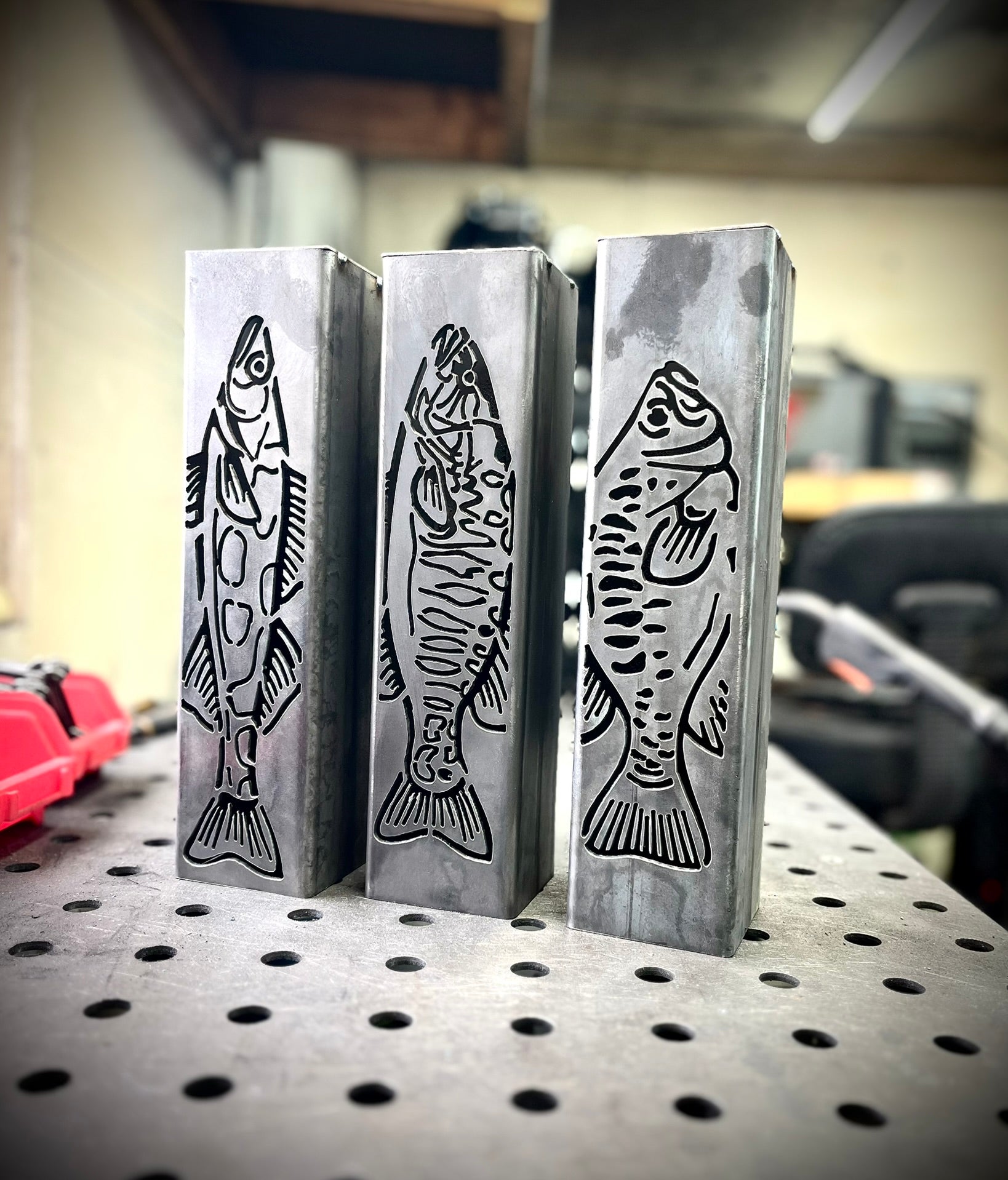 Three metal garden column pillars with fish designs on a workshop table.