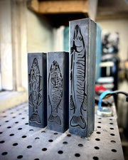 Three garden column pillars with fish designs on a workshop table.