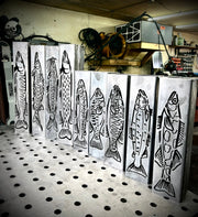 Metal garden column pillars with fish designs on a pegboard in a workshop setting