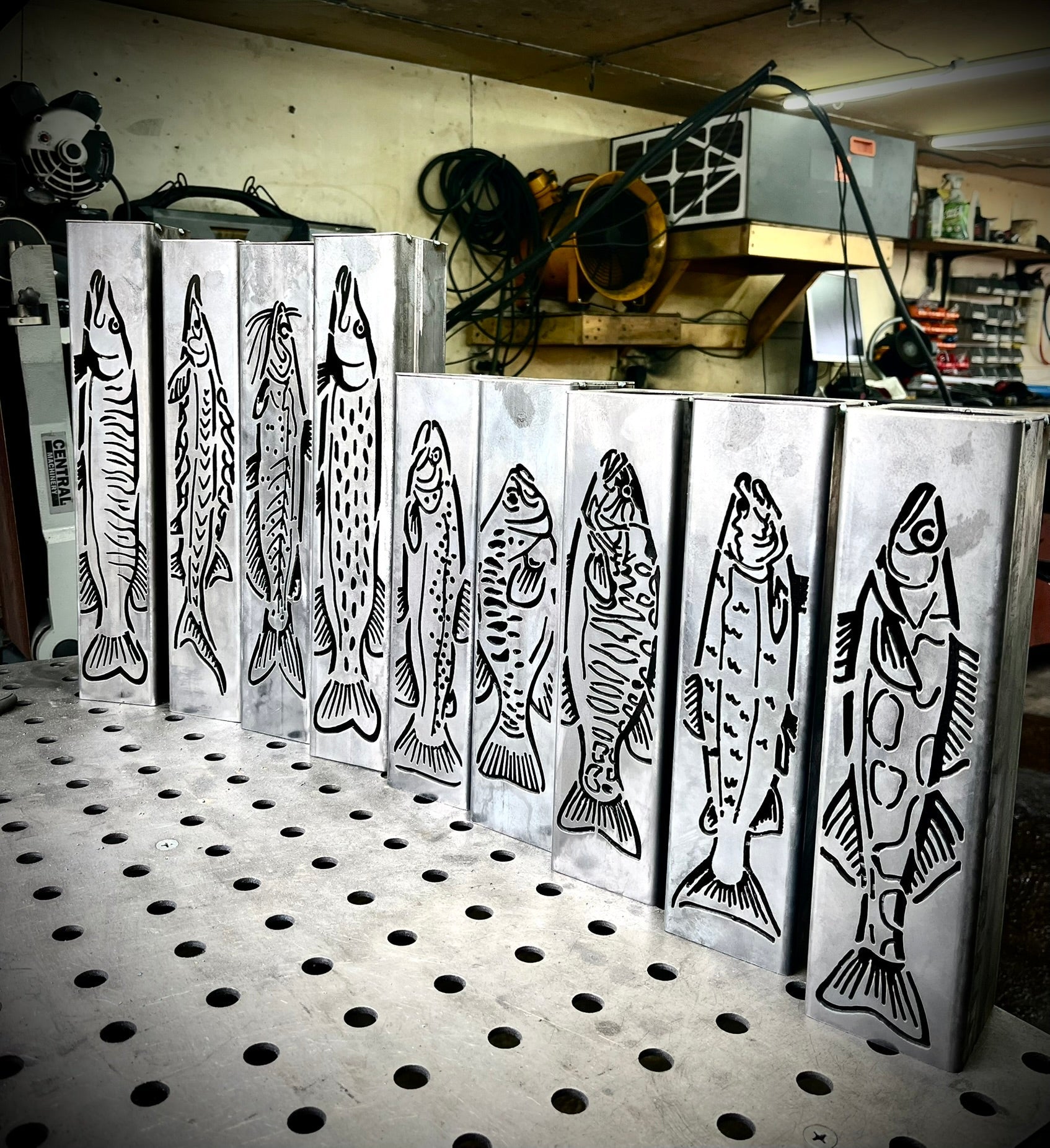 Metal garden column pillars with fish designs on a pegboard in a workshop setting