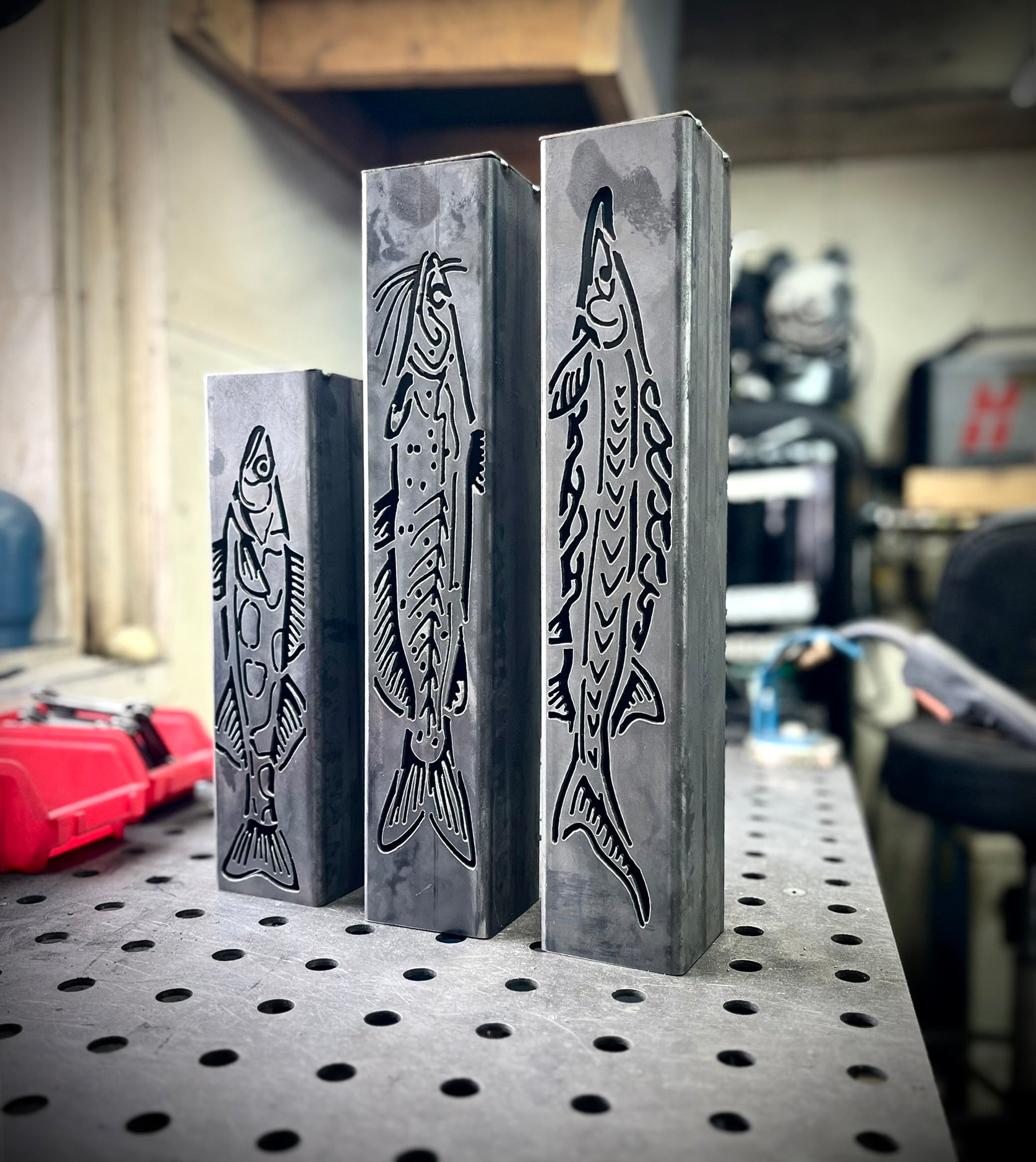 Three metal garden column pillars with fish designs on a workshop table.