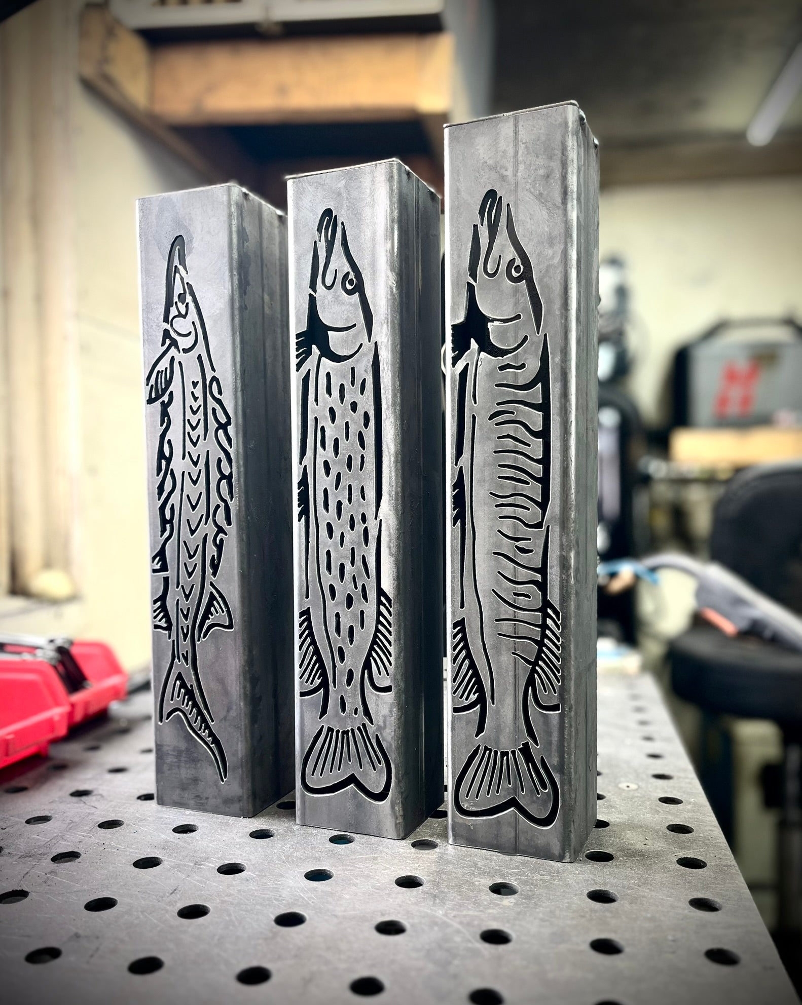 Three metal garden column pillars with fish engravings on a workshop table.