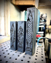 Three metal garden column pillars with fish designs on a metal surface.