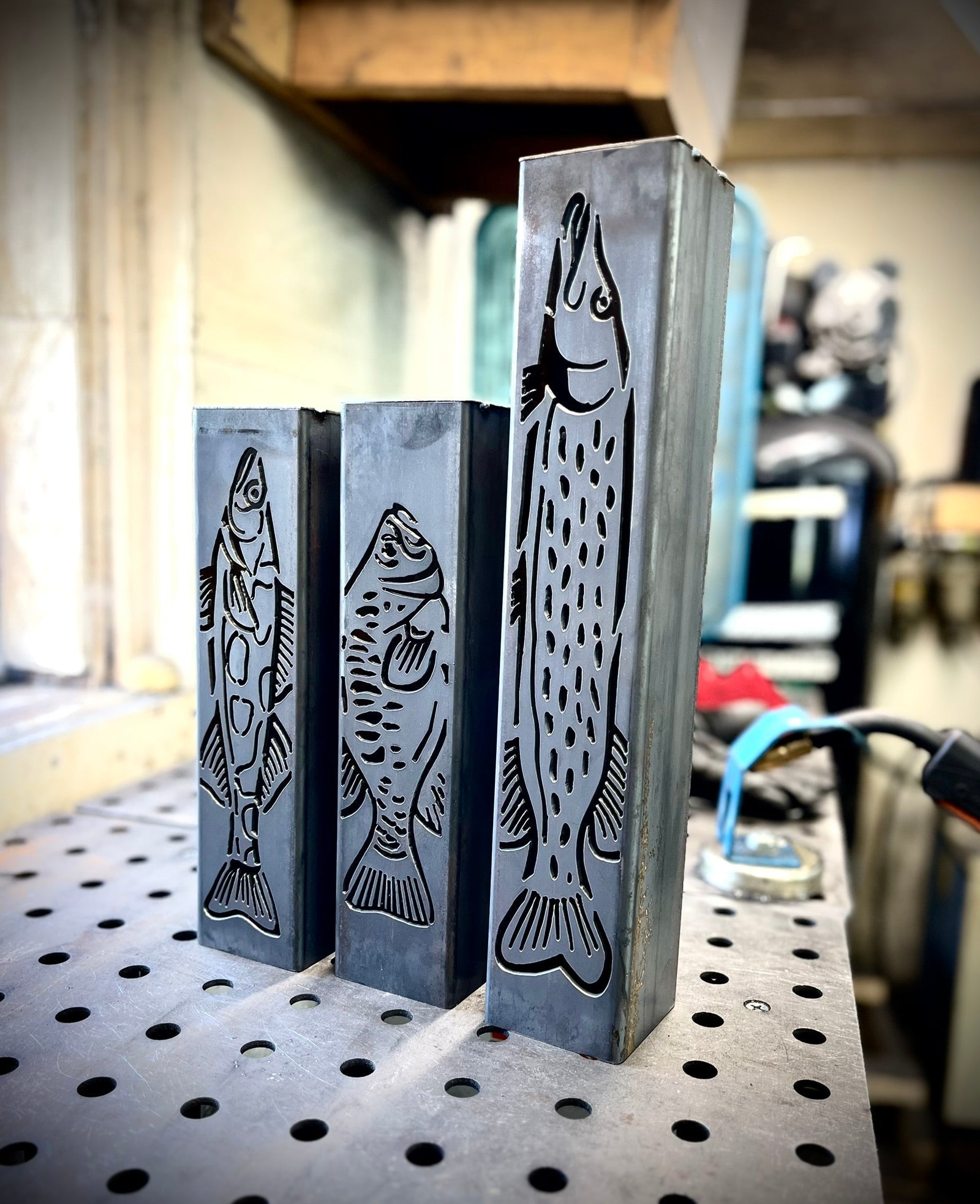 Three metal garden column pillars with fish designs on a metal surface.