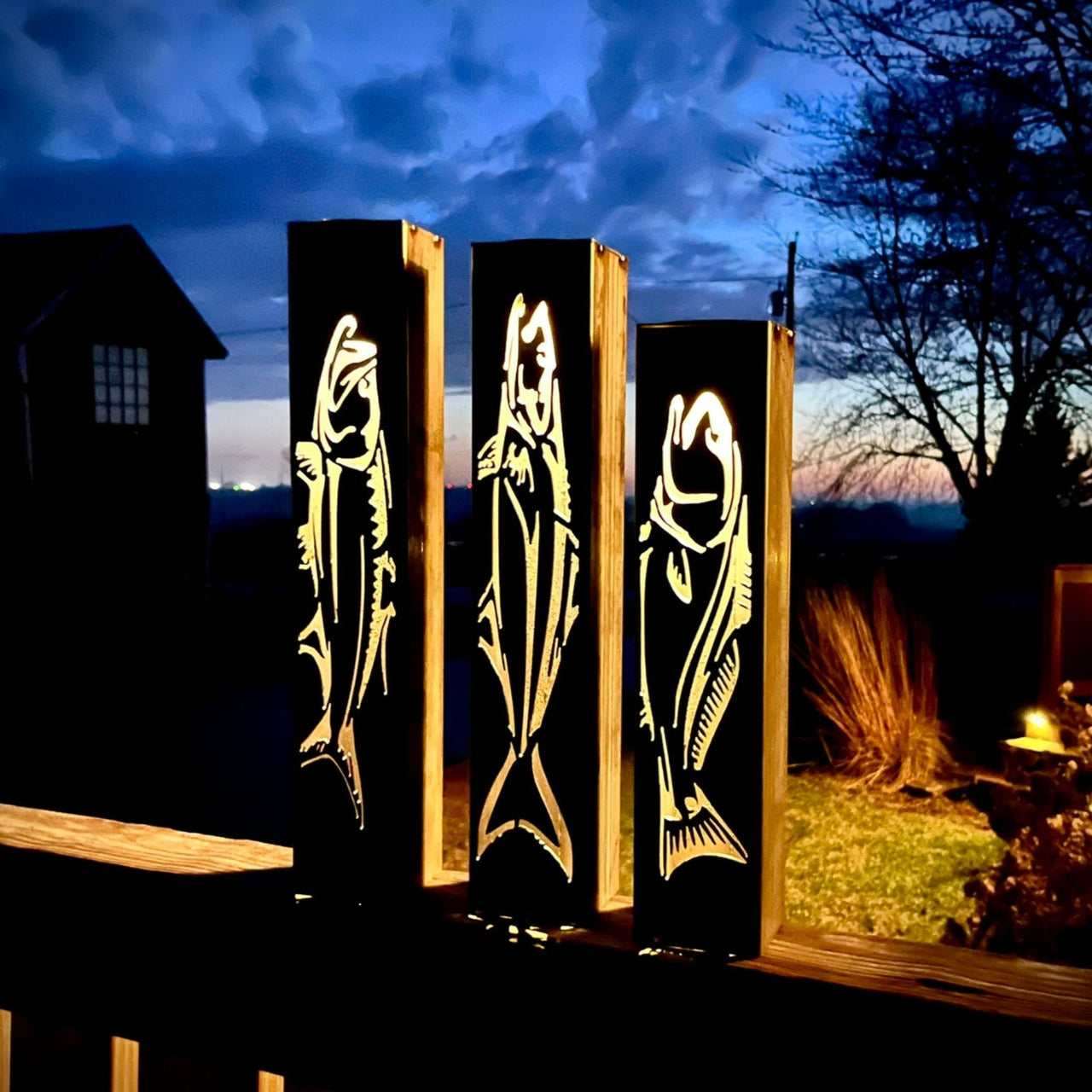 Three illuminated garden pillars with fish designs against a night sky.