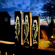 Three illuminated garden pillars with fish designs against a night sky.