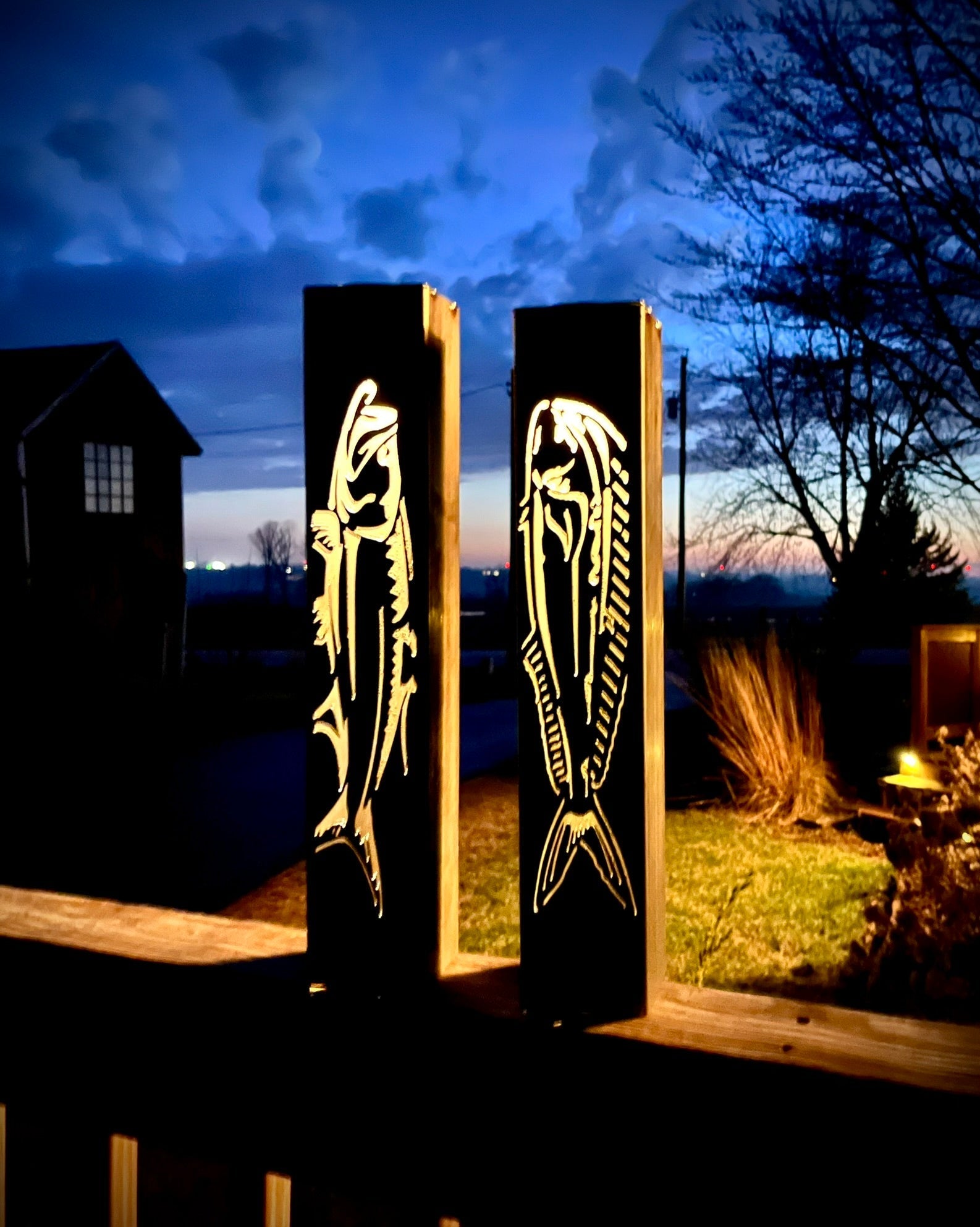 Two illuminated garden pillars with fish designs against a night sky.