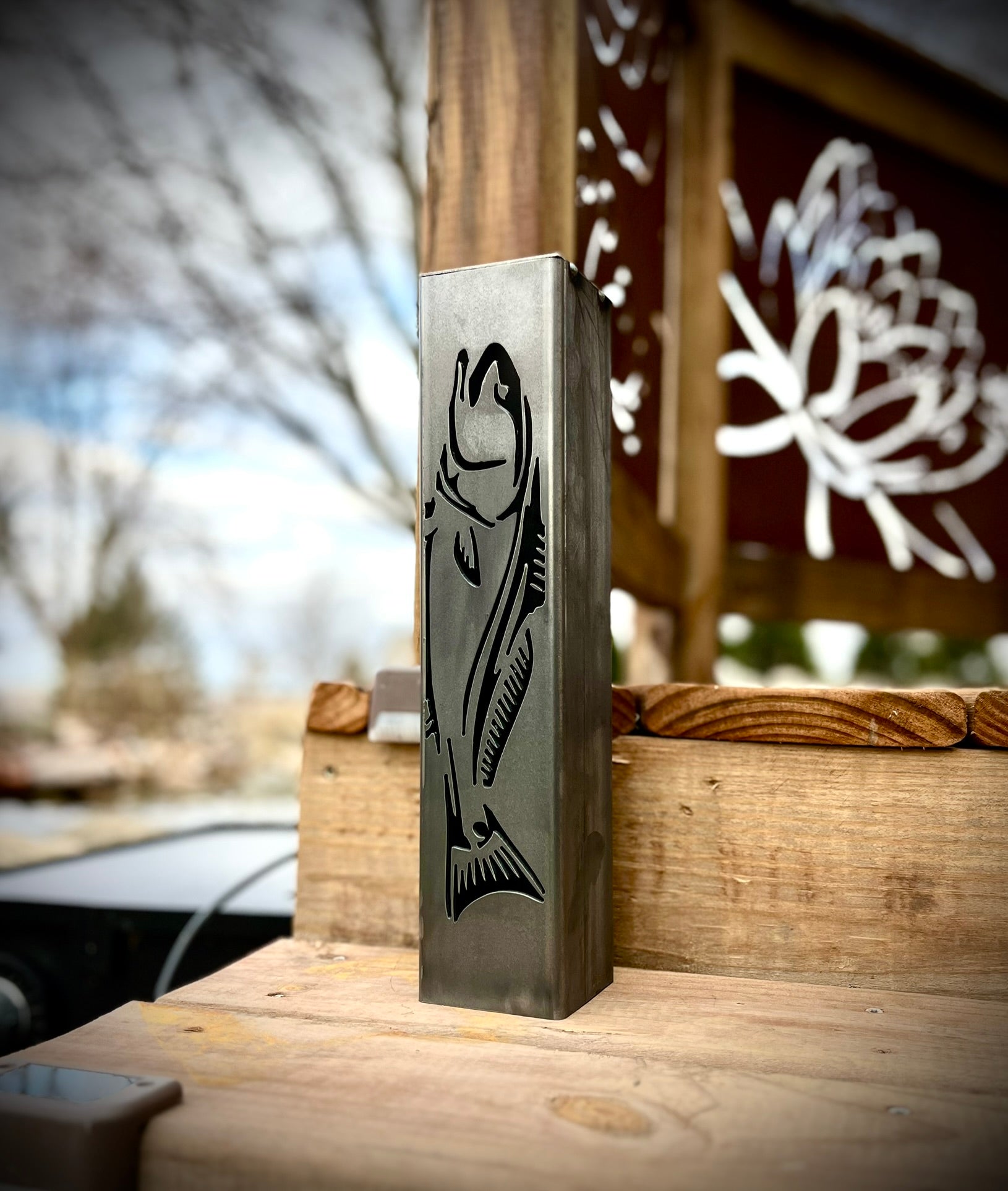Metal garden pillar with fish design on a wooden surface outdoors