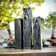 Three metallic fish garden column pillars on a wooden surface with a blurred natural background