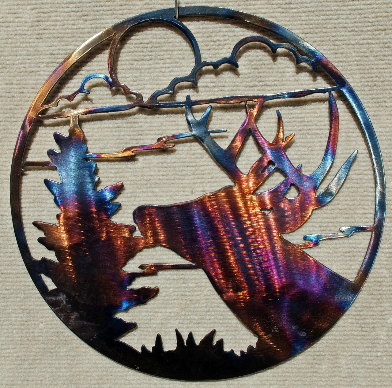 Metal art piece with a deer and antlers design on a textured beige background