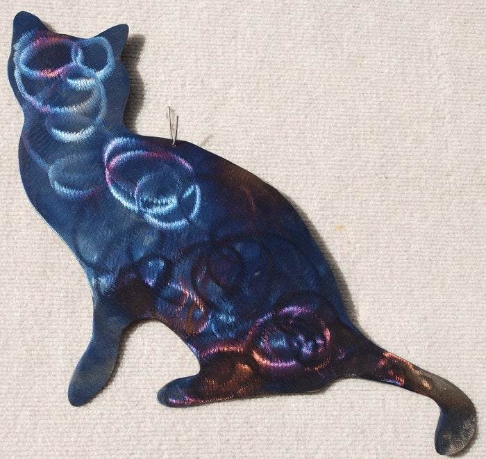 Cat-shaped ornament with metallic blue and purple finish on a beige fabric background