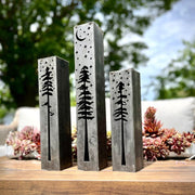 Three metal pillars with engraved tree designs on a wooden surface outdoors.