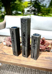 Three metal pillars with tree designs on a wooden surface outdoors.