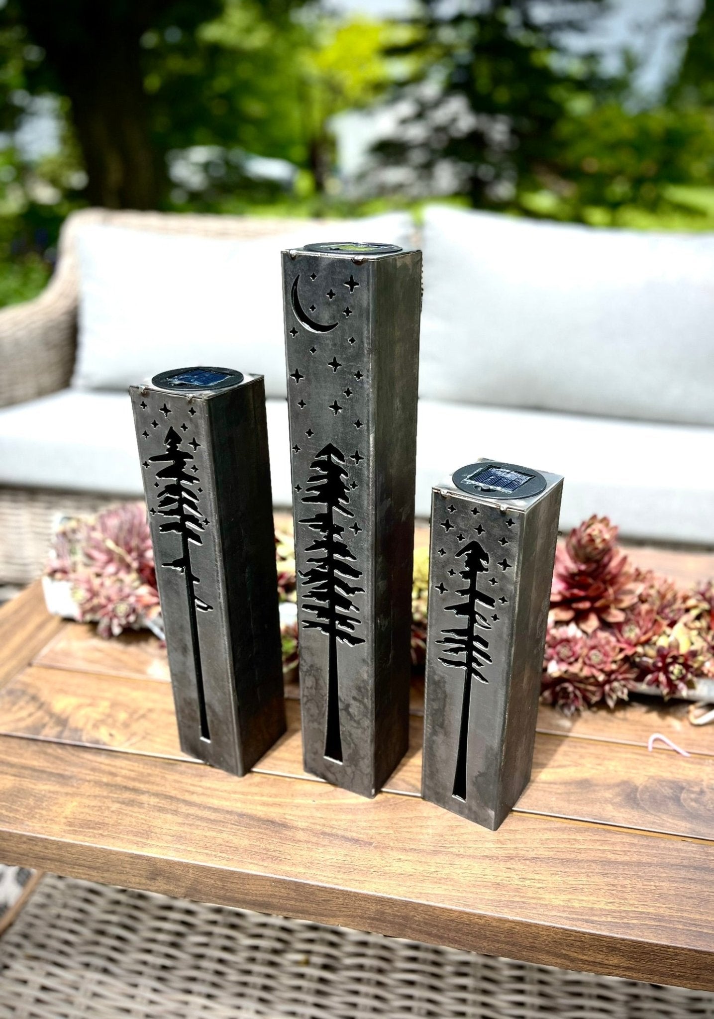 Three metal pillars with tree designs on a wooden surface outdoors.