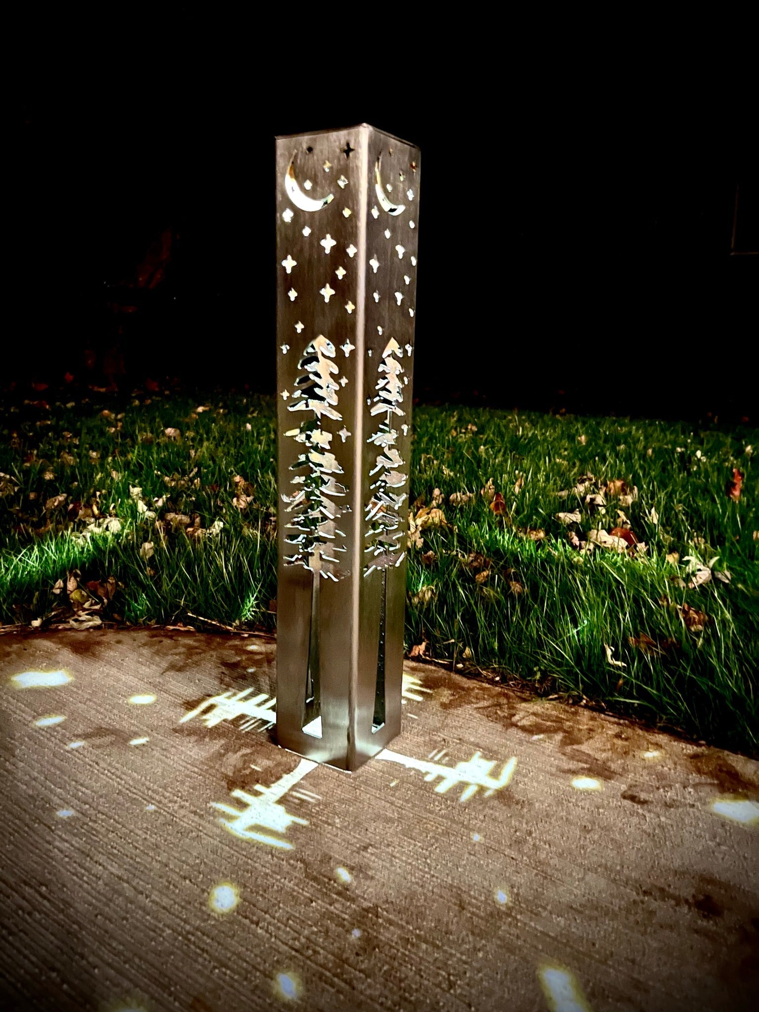 Decorative outdoor garden column with engraved designs on a grassy area at night.