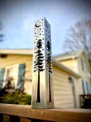 Decorative garden column with cut-out designs on a wooden surface outdoors.
